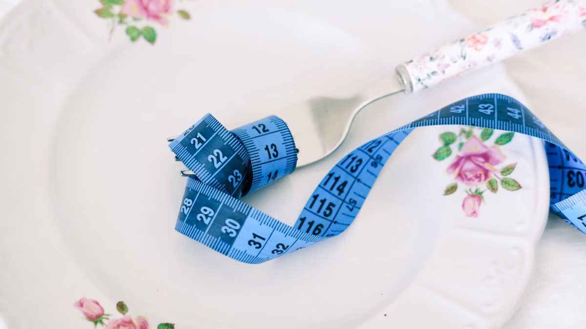 A floral plate with a fork and blue measuring tape symbolizing dieting or healthy eating.